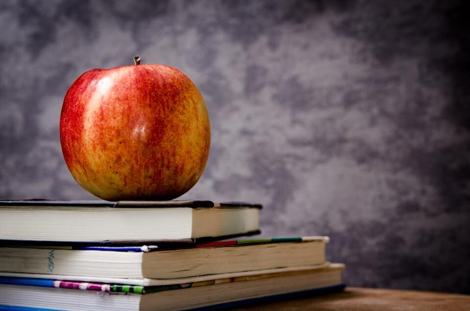 Una mela rossa appoggiata su una pila di libri di scuola